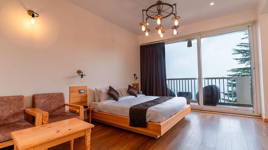 A bedroom with a white bed, a rug, and large windows, interior setting - Clarks Exotica Resort, Near Mukhteshwar.