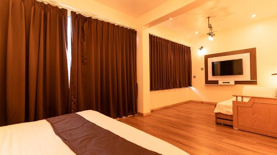 A bedroom with a bed, a couch, and a television, warm lighting, interior setting - Clarks Exotica Resort, Near Mukhteshwar.