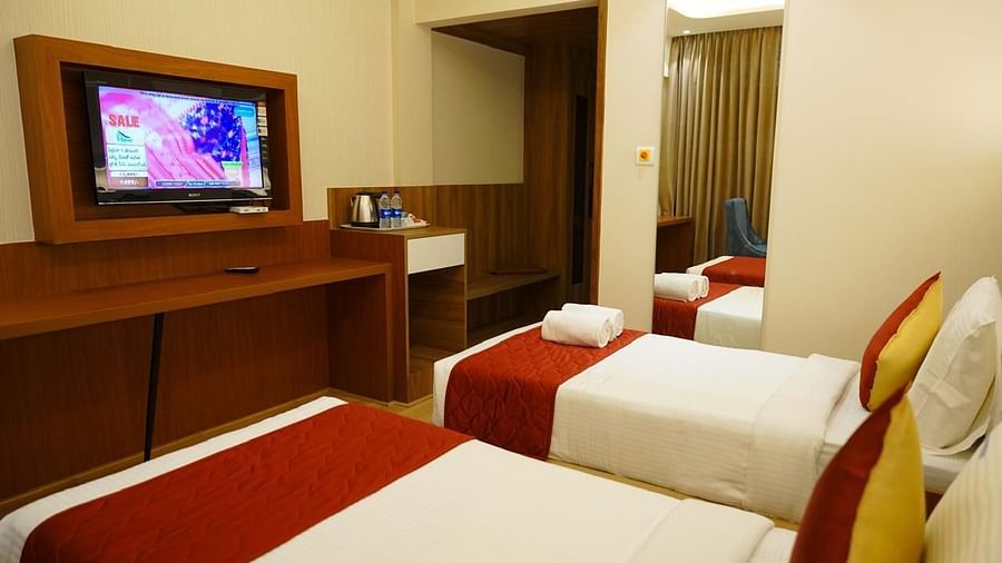 TV unit and twin beds in a well-lit room at Kalyan Residency Hotel, Tirupati – a perfect blend of comfort and style.