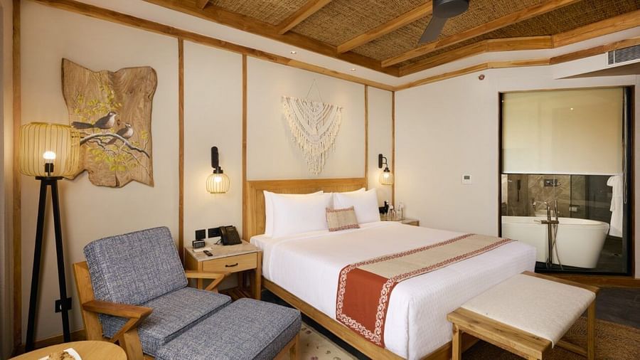 Room with a double bed, cosy lounge chair, floor lamp, and wooden ceiling fan - Royal Tulip, Chitwan