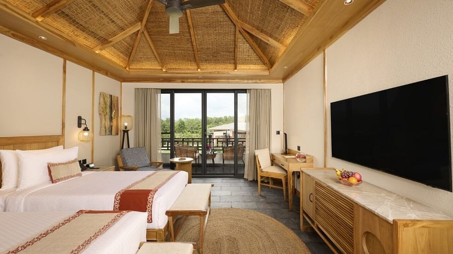 Spacious room with twin beds, television, fan, balcony, and wooden decor accents - Royal Tulip, Chitwan