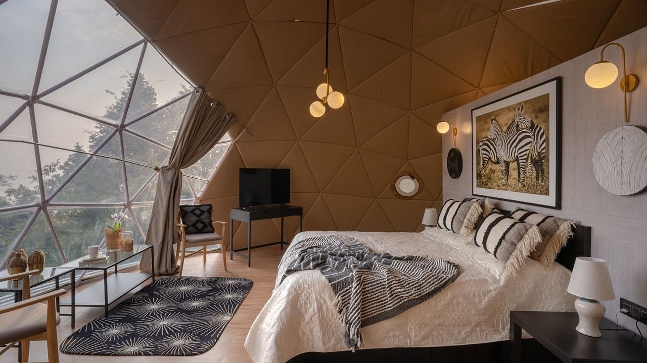 An image of a bedroom in dome cottage with king size bed, bedside table, flat TV screen, chandeliers, etc. | Avalon Cottages, Kanatal