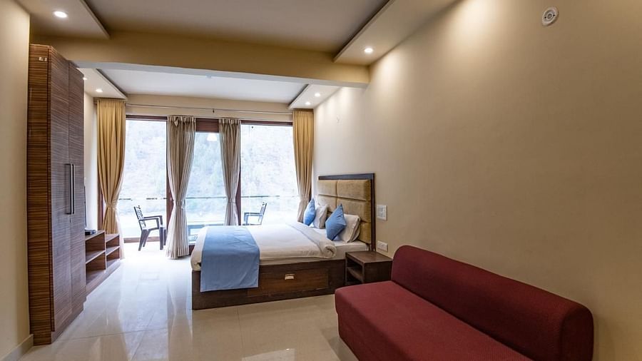 Spacious room featuring a bed, wall-mounted TV, sofa, and balcony view through glass doors.