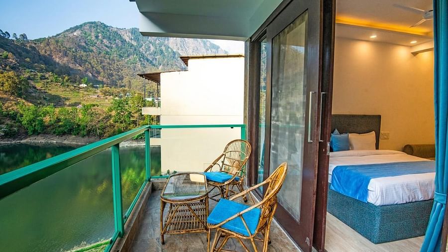 Balcony with blue-cushioned chairs and a table facing a forest-lined lake.