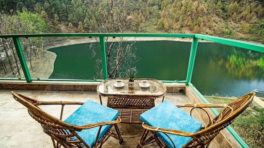 Balcony with blue-cushioned chairs and a table facing a forest-lined lake.