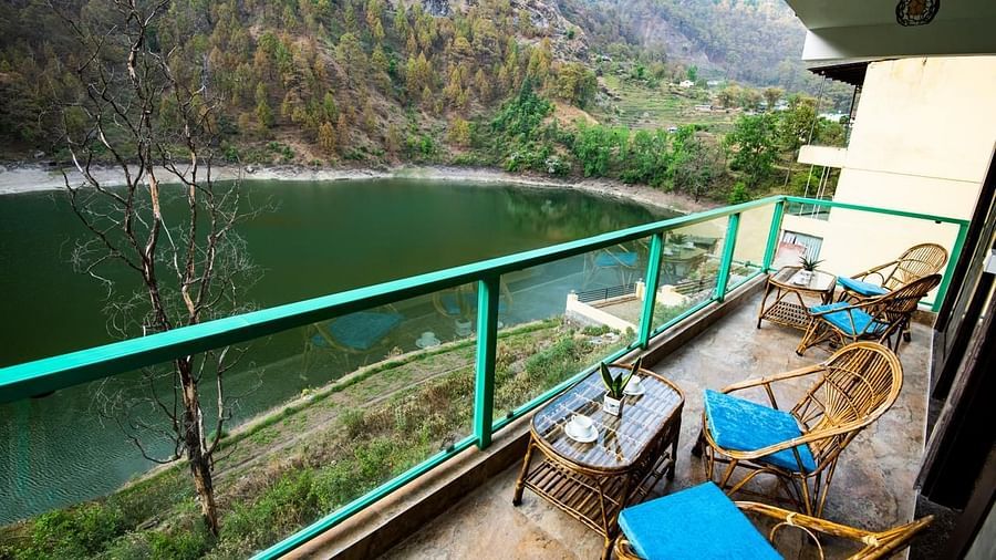 Balcony with blue-cushioned chairs and a table facing a forest-lined lake.