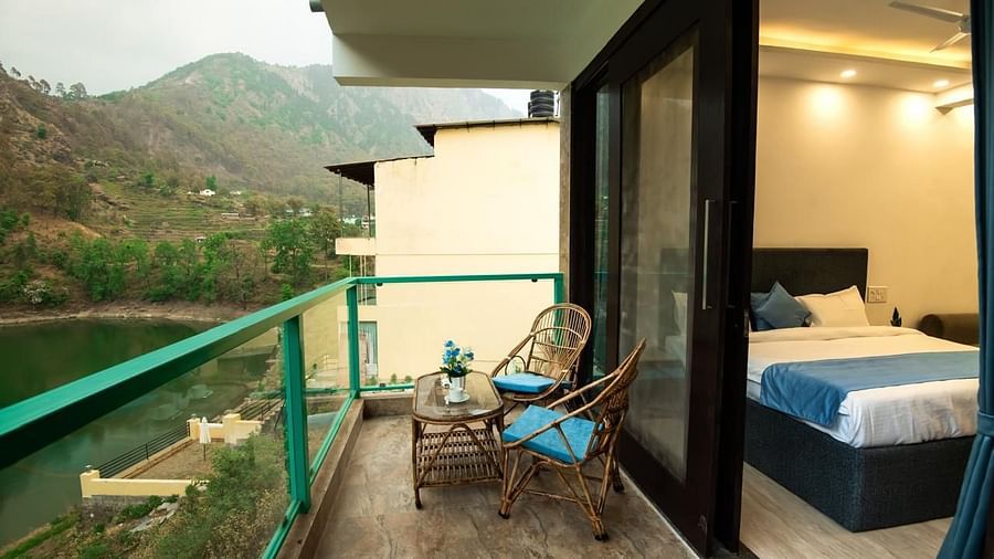 A bedroom with an attached balcony featuring two chairs and a table, overlooking green hills and a scenic mountain view.