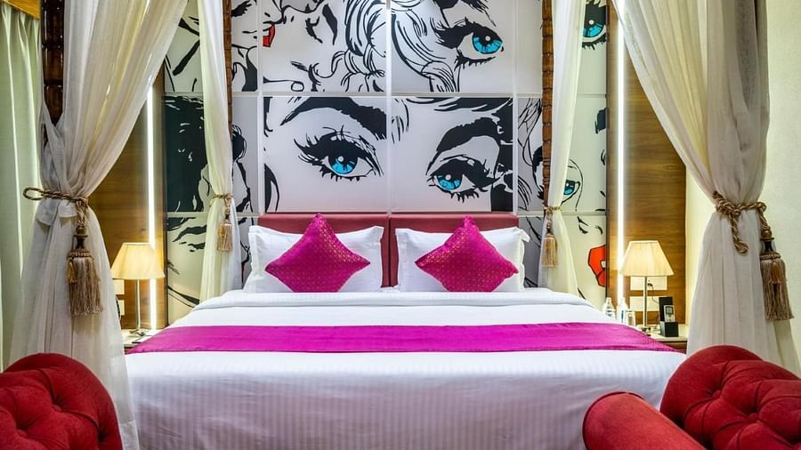 A view of the spacious bed from the foot, with a neatly made bed and posters above the headboard at Angel Lords Eco Inn, Amreli.