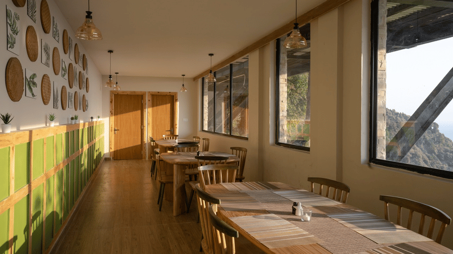 A dining area with several chairs and table placed at one side with widows| Avalon Cottages, Kanatal