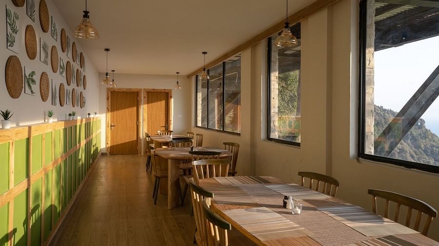 An image of a dining area with several chairs and table placed at one side with widows| Avalon Cottages, Kanatal