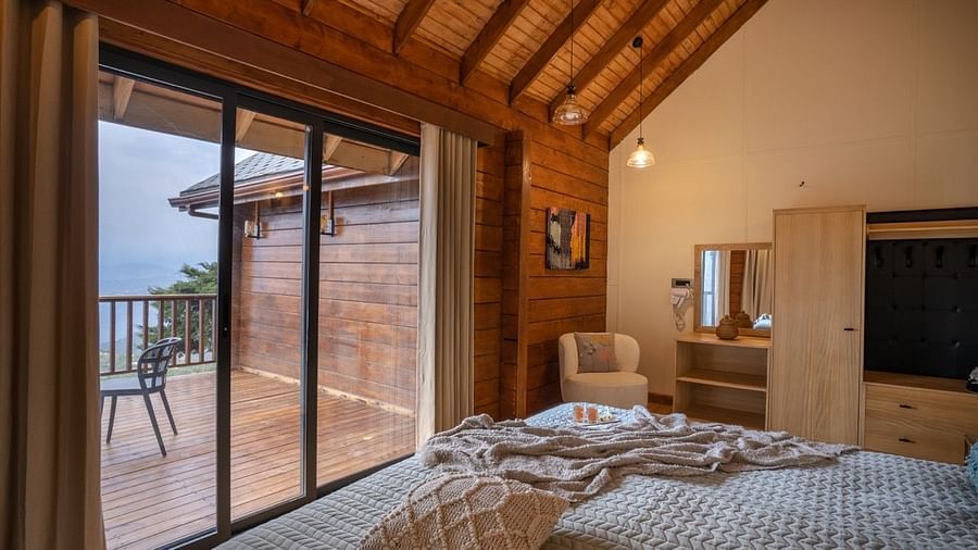 An image of a bedroom leading to the patio with woodden ceiling | Avalon Cottages, Kanatal
