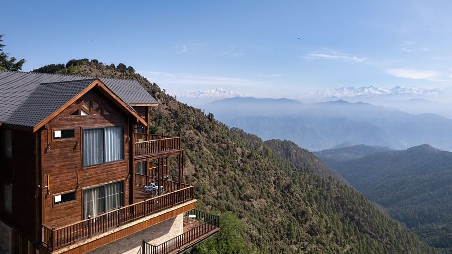 A view of a cottage and the balcony with a backdrop of mountains and clouds | Avalon Cottages, Kanatal