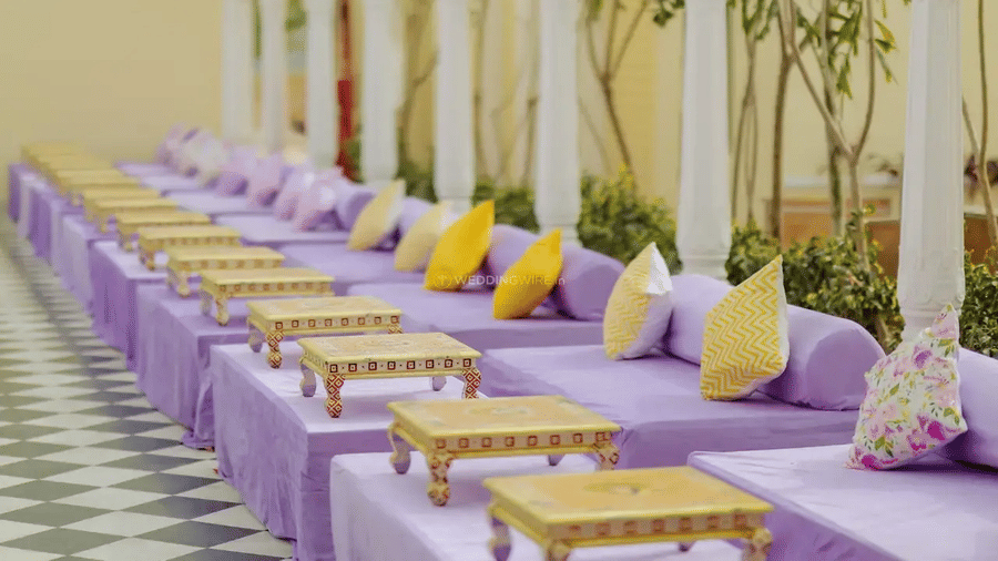 A row of low tables with purple coverings and yellow and white cushions along a corridor at Beelwa Palace, Jaipur.