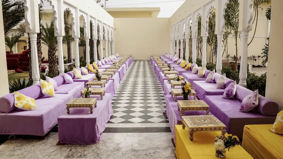 Long seating arrangement with low sofas and cushions lined along pillars at Beelwa Palace, Jaipur