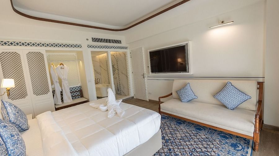 Corner view shot of the bedroom at Ananata Room featuring a plush double bed alon with a television and a couch in front of it at Bhagirathi by RDB Atishay.