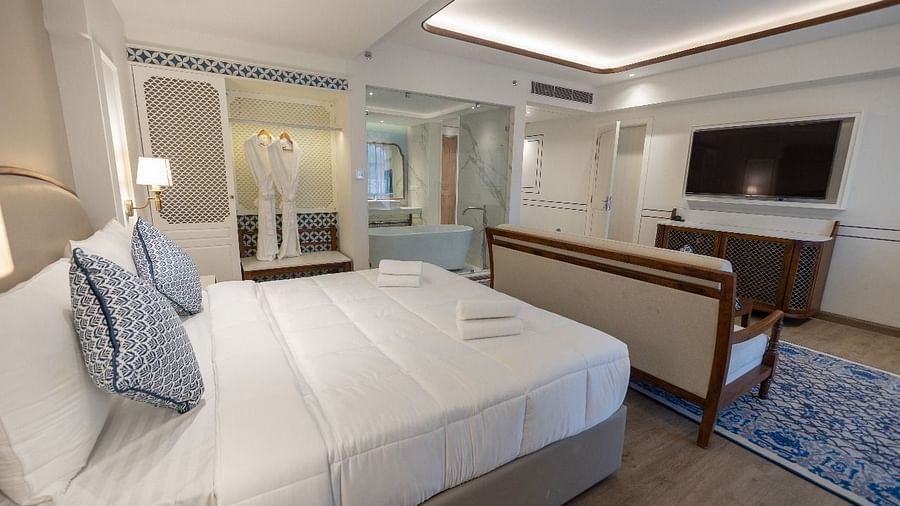 Corner view shot of the Purna room featuring a soft double bed with neatly arranged cushions along with a wall mounted television at Bhagirathi by RDB Atishay.