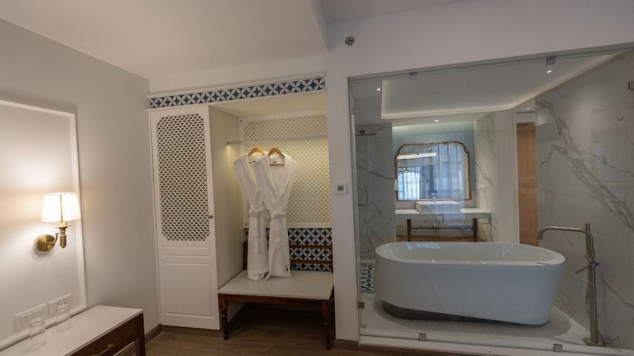 A bathtub in the bathroom of the Purna Room separated by a glass partition alongside a wardrobe at Bhagirathi by RDB Atishay. 