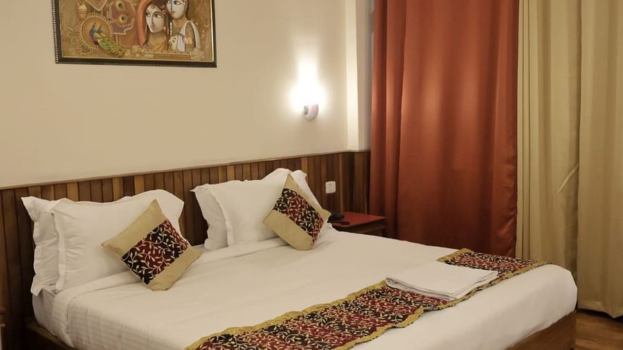An image of the super deluxe room at Sumitel Chiminda, Pelling featuring a queen size bed, bed side table, decorative lighting, and a painting hung on the wall