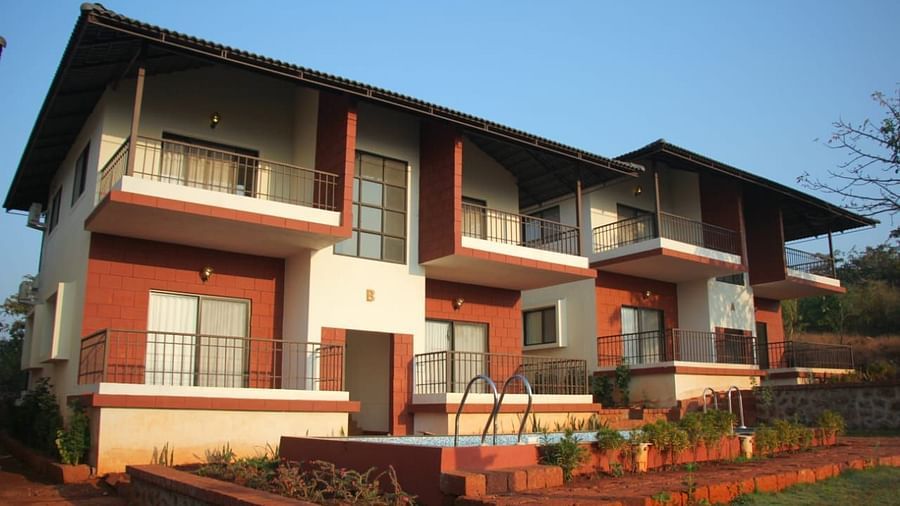 A two-story building with white walls and burgundy accents, featuring a swimming pool under a clear blue sky.