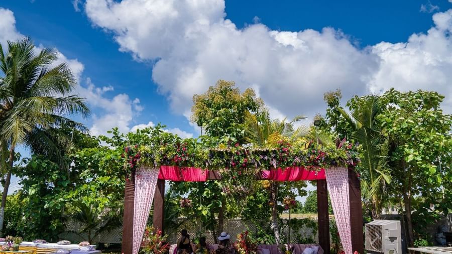 An outdoor wedding canopy or mandap decorated with pink and white fabrics and flowers, set on a green lawn under a bright blue sky | Grande Pavillion | Grand Bay Resort and Spa