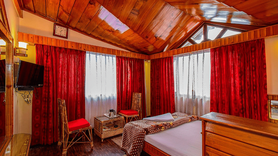 Hotel room with a wooden vaulted ceiling, a double bed, red curtains, and a wall-mounted television at Hotel Dolphin Darjeeling.
