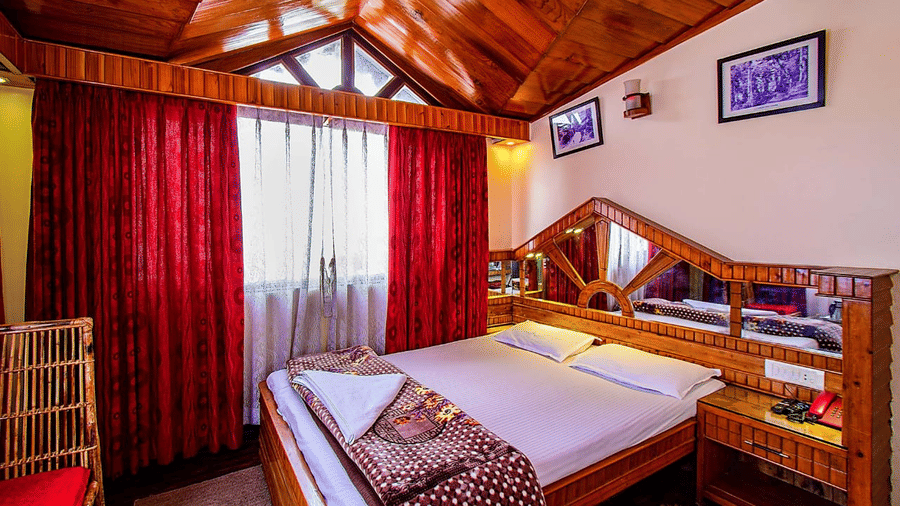 Room featuring a wooden vaulted ceiling, double bed, red curtains, and a wooden dressing table with a large mirror at Hotel Dolphin Darjeeling.
