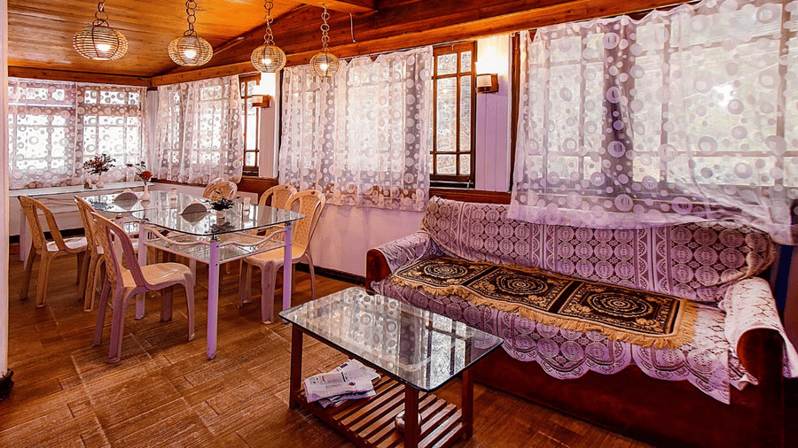 Restaurant/dining room with lace curtains, wooden walls and ceiling, glass tables, and light-coloured chairs at Hotel Dolphin Darjeeling.