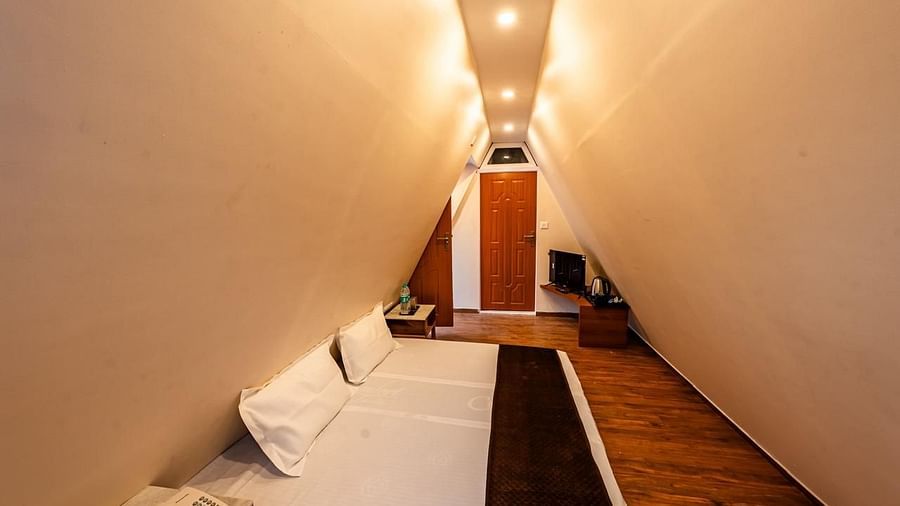 A hotel room with angled walls creating a narrow appearance, a bed, and a television visible at the far end.