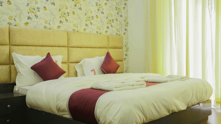 Bedroom of Lime Tree Hotels & Service Apartment Private Limited featuring a floral patterned headboard, maroon cushions, and yellow curtains.