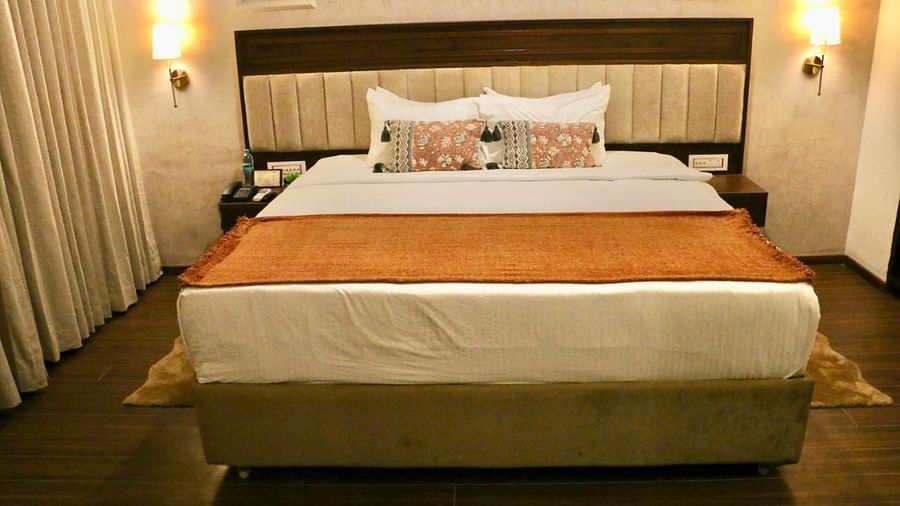 A neatly made bed with white and orange linens of Luxury Junior Suite at Nalapad Hotel Bangalore International.