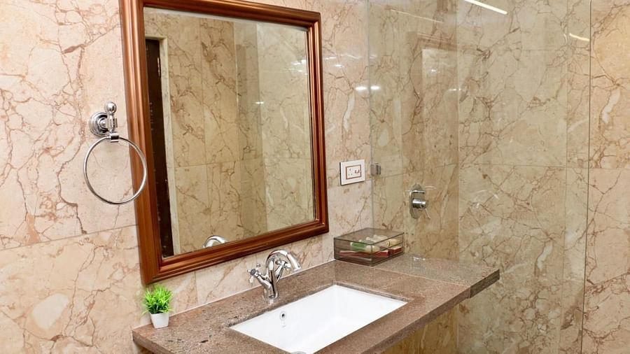 A bathroom featuring a sink with a brown countertop, a mirror, and beige marble walls of Luxury Junior Suite at Nalapad Hotel Bangalore International.
