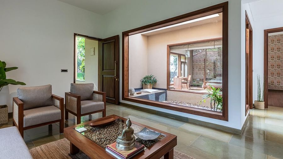 A living room with armchairs, a coffee table, and large glass doors leading to a patio - Shreyas Retreat