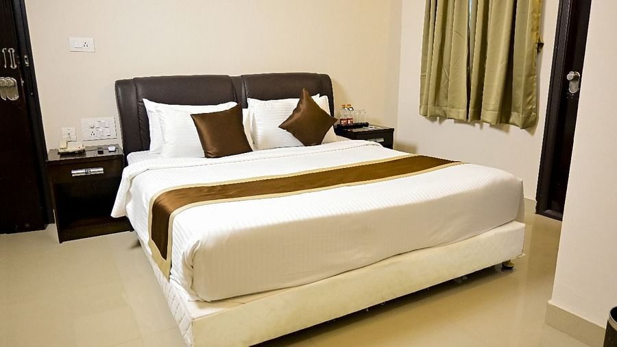  A comfortable hotel room at TGI Livancia Hillside, JC Nagar, Mysore, with a neatly made double bed, bedside tables with lamps, and curtains on the window.