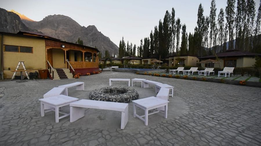 A bonfire setting with white seating area surrounded by buildings at White Sands Resort, Ladakh.
