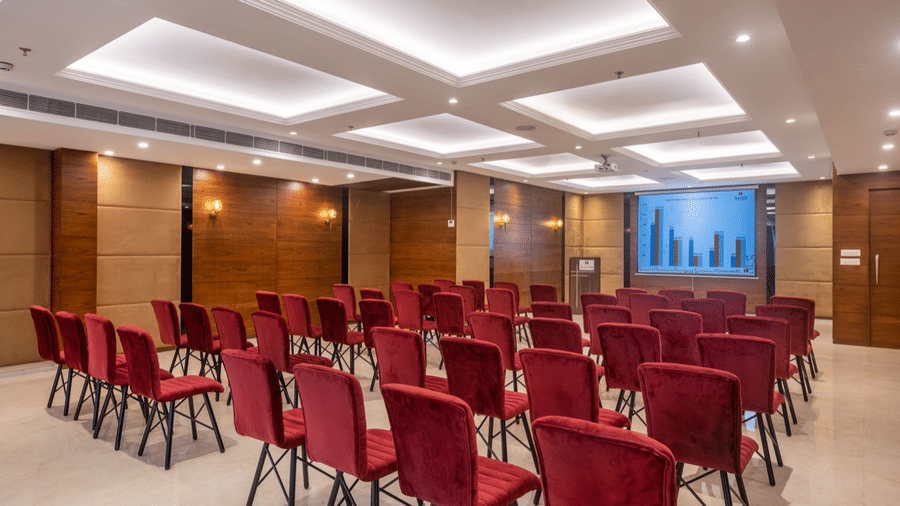 Mid-size conference room with rows of red chairs facing a presentation screen.