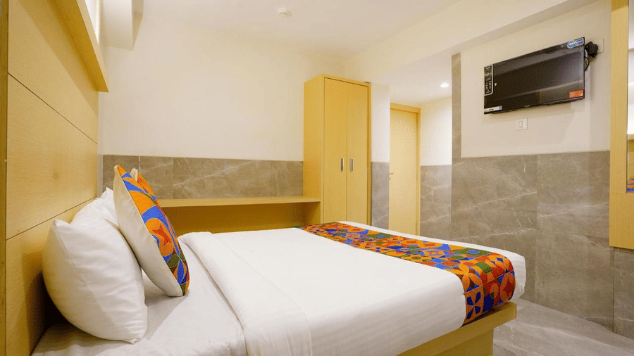 A minimalistic modern designed room with a twin size bed, featuring colourful bed runner and cushions, wooden furniture and a mounted T.V. at Shyanu Lords Eco Inn Airoli.