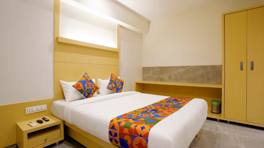 A well furnished room with a twin size bed featuring colourful bed runner and cushions, bedside drawers and a wardrobe at Shyanu Lords Eco Inn Airoli.
