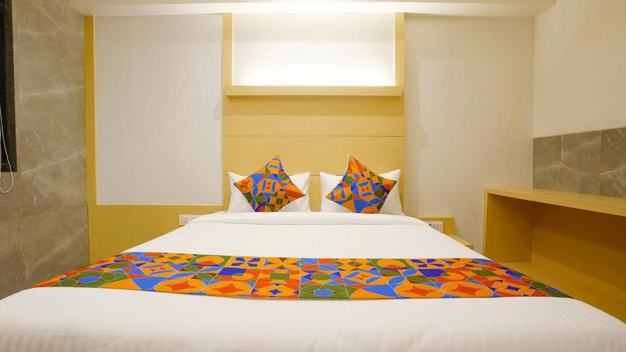 An elegant room with a twin size bed, colourful bed runner and cushions and wooden furniture at Shyanu Lords Eco Inn Airoli.