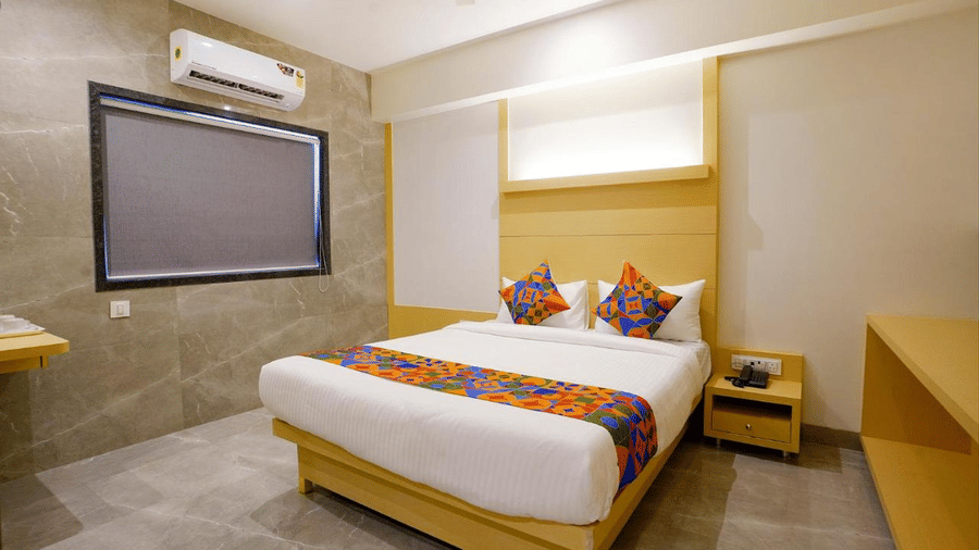 A side view of a well furnished room featuring a twin size bed, bedside drawers, wooden furniture and a projector screen at Shyanu Lords Eco Inn Airoli.