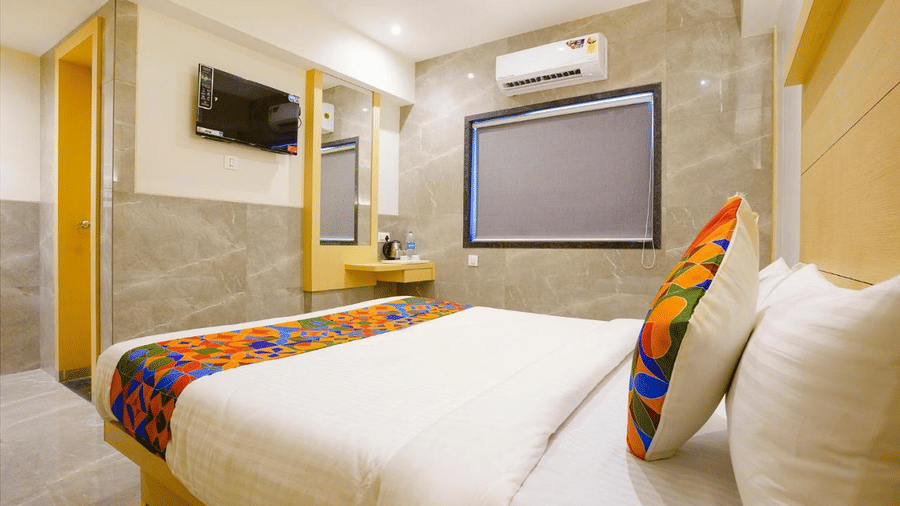 An elegant well furnished room with a twin size bed, colourful cushion and a runner, a wall mirror and a projector screen at Shyanu Lords Eco Inn Airoli.