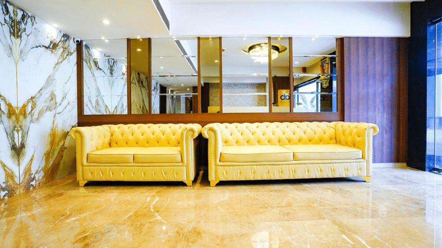 Modern designed lounge area with elegant yellow sofas and mirrored wall panels at Shyanu Lords Eco Inn Airoli.