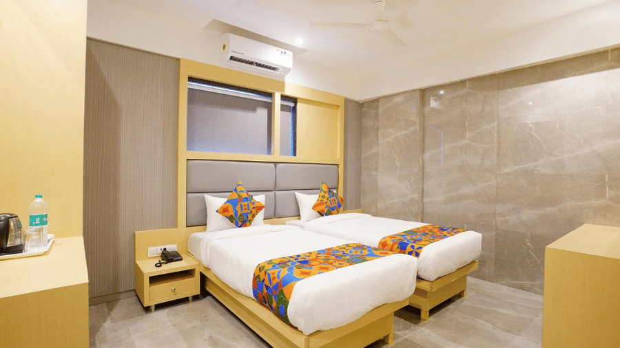 An elegant room with two single beds, colourful pillows and a runner, bedside drawers and wooden furniture at Shyanu Lords Eco Inn Airoli.