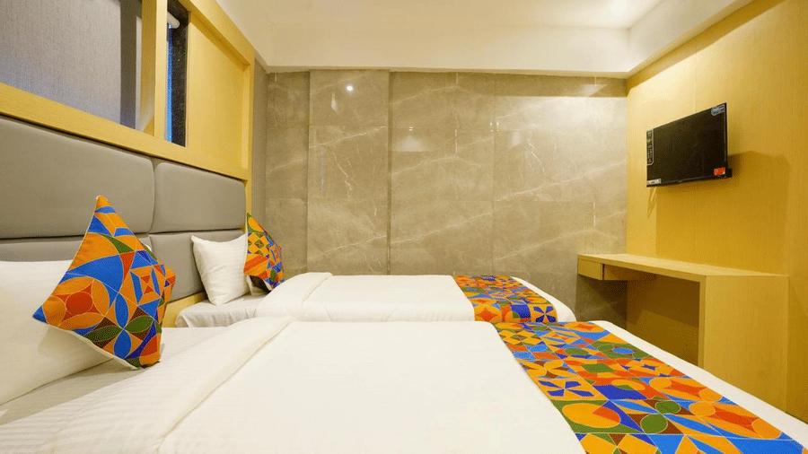 A well furnished room with two beds, colourful pillows and a runner, wall-mounted T.V. at Shyanu Lords Eco Inn Airoli