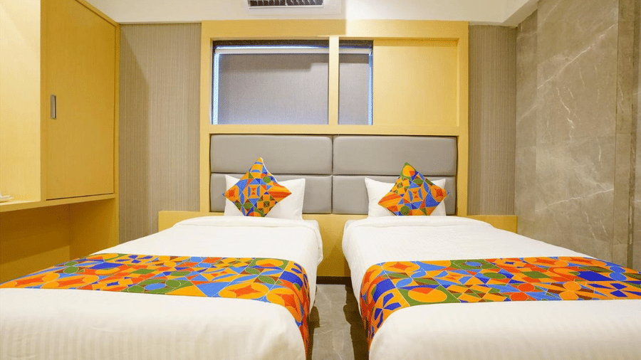 A wooden furnished room with two single beds, colourful pillows and a runner, and a wardrobe at Shyanu Lords Eco Inn Airoli.