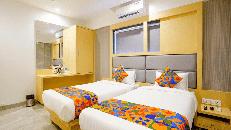 A twin room featuring two single bed, colourful cushions and a runner, wooden furniture and a dustbin at Shyanu Lords Eco Inn Airoli.