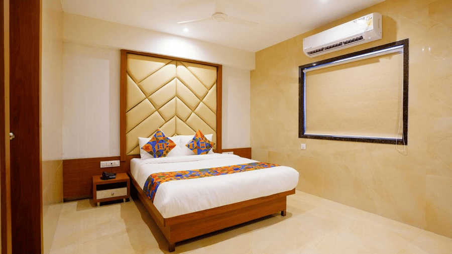 Modern designed room featuring a twin size bed with colourful pillows and a runner, patterned headboard, bedside drawers and a projector screen space at Shyanu Lords Eco Inn Airoli.