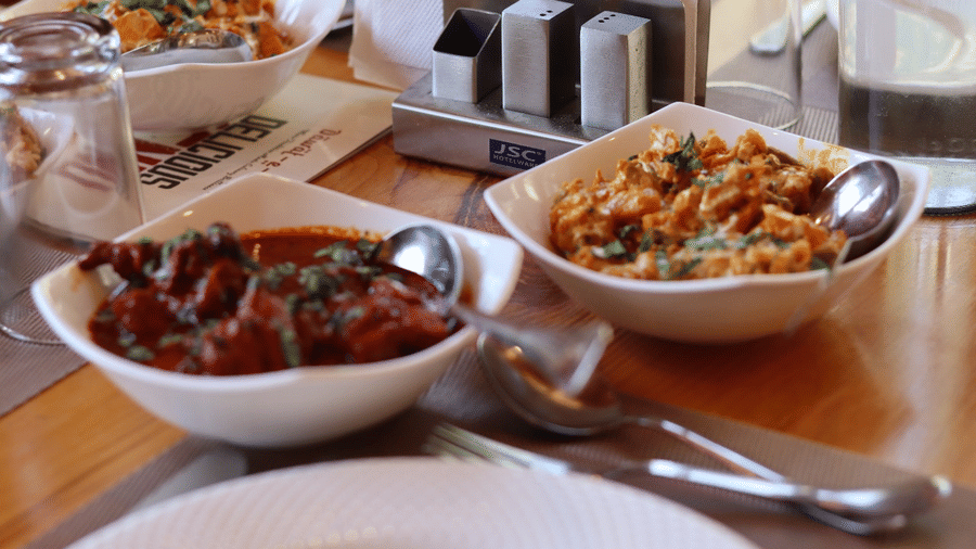 Dishes of food served in bowls on a wooden table alongside cutlery and condiments at Dawat e Drung by FrozenFall Resort, Drung, Tangmarg.