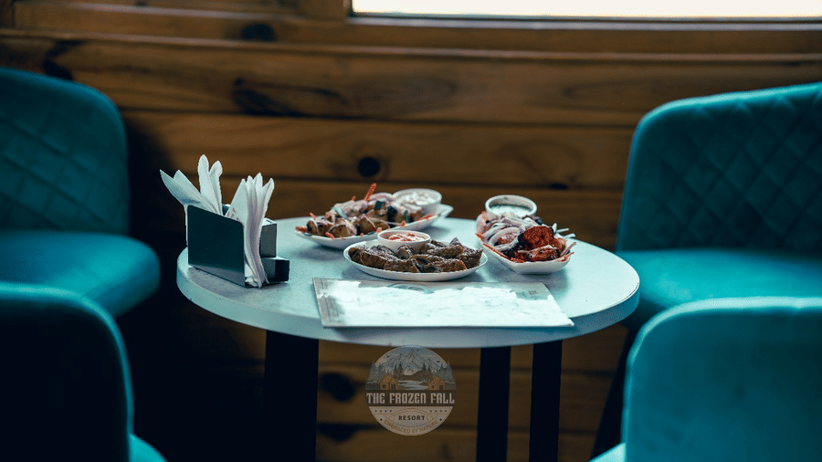 A seating arrangement at Dawat e Drung by FrozenFall Resort, Drung, Tangmarg, with chairs around 1 round table featuring menus and small plates.