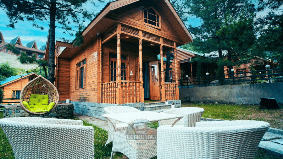 A garden patio area at Dawat e Drung by FrozenFall Resort, Drung, Tangmarg, with 4 white chairs, 1 table and a hanging egg chair structure.