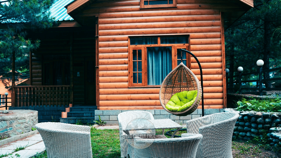 Outside a log cabin villa at Dawat e Drung by FrozenFall Resort, Drung, Tangmarg, featuring an outdoor seating table and a hanging egg chair.